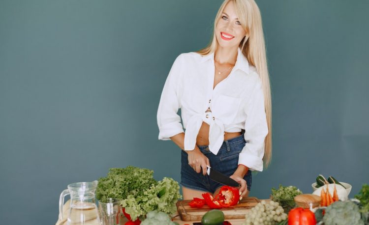 A smiling blonde woman chops vegetables, promoting healthy eating and lifestyle.