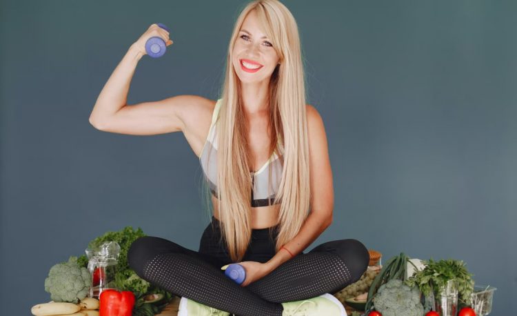 Woman lifting a small dumbbell while surrounded by fresh vegetables, embodying health and fitness.